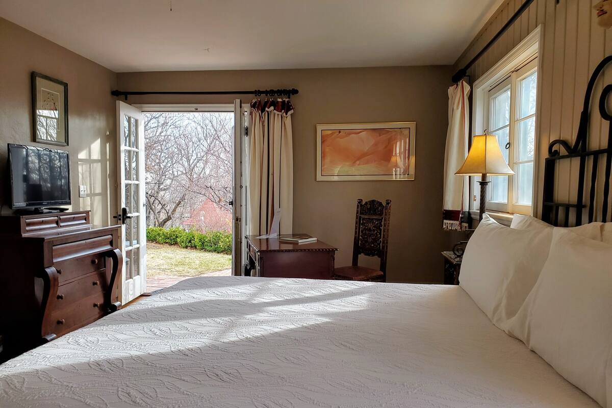 A hotel room with a large bed, a desk with a chair, a television, a window with curtains, and a painting on the wall.