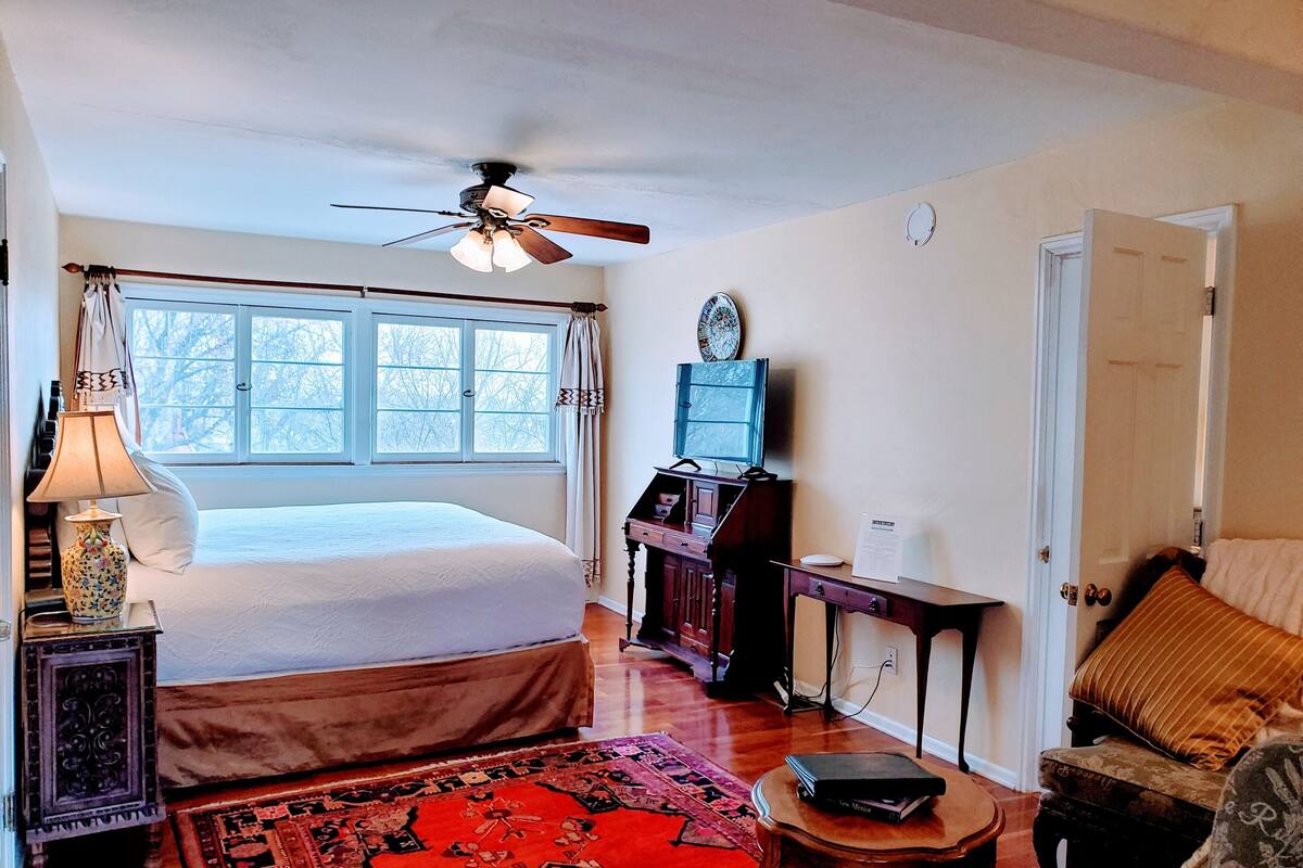 A bedroom with a bed, a ceiling fan, a window, a desk, a chair, and a rug.