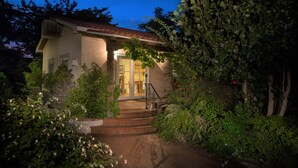 Una casa con techo de tejas, una entrada con escalones y un jardín con diversas plantas.