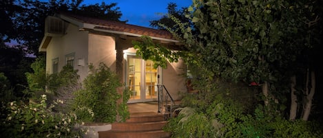 Uma casa com telhado de telhas, entrada frontal com degraus e jardim com diversas plantas.