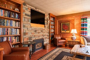 A cozy living room with a fireplace, leather furniture, a bookshelf, and a flat-screen TV mounted on a brick wall.