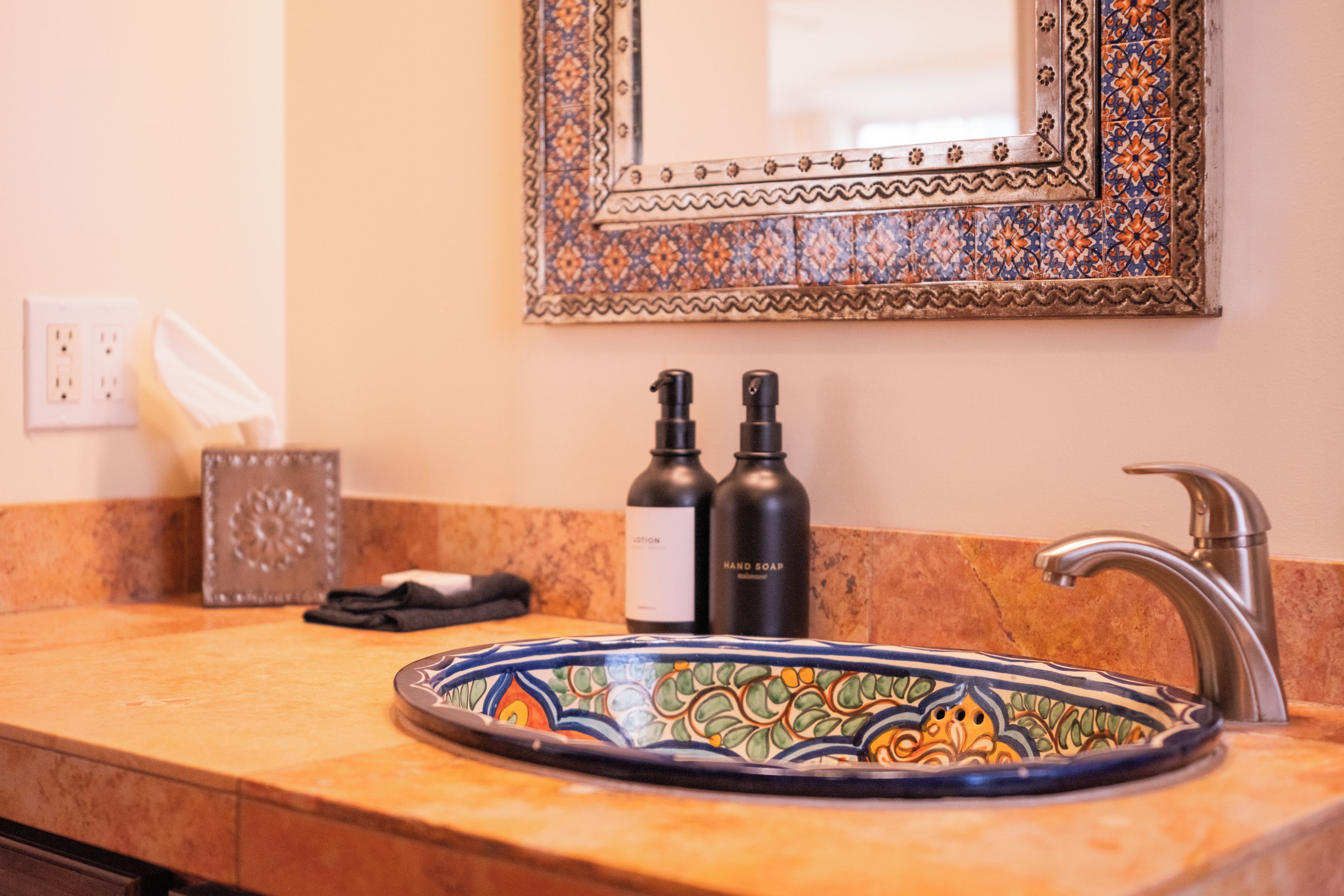A bathroom with a decorative sink, a mirror with a patterned frame, and toiletries on the counter.