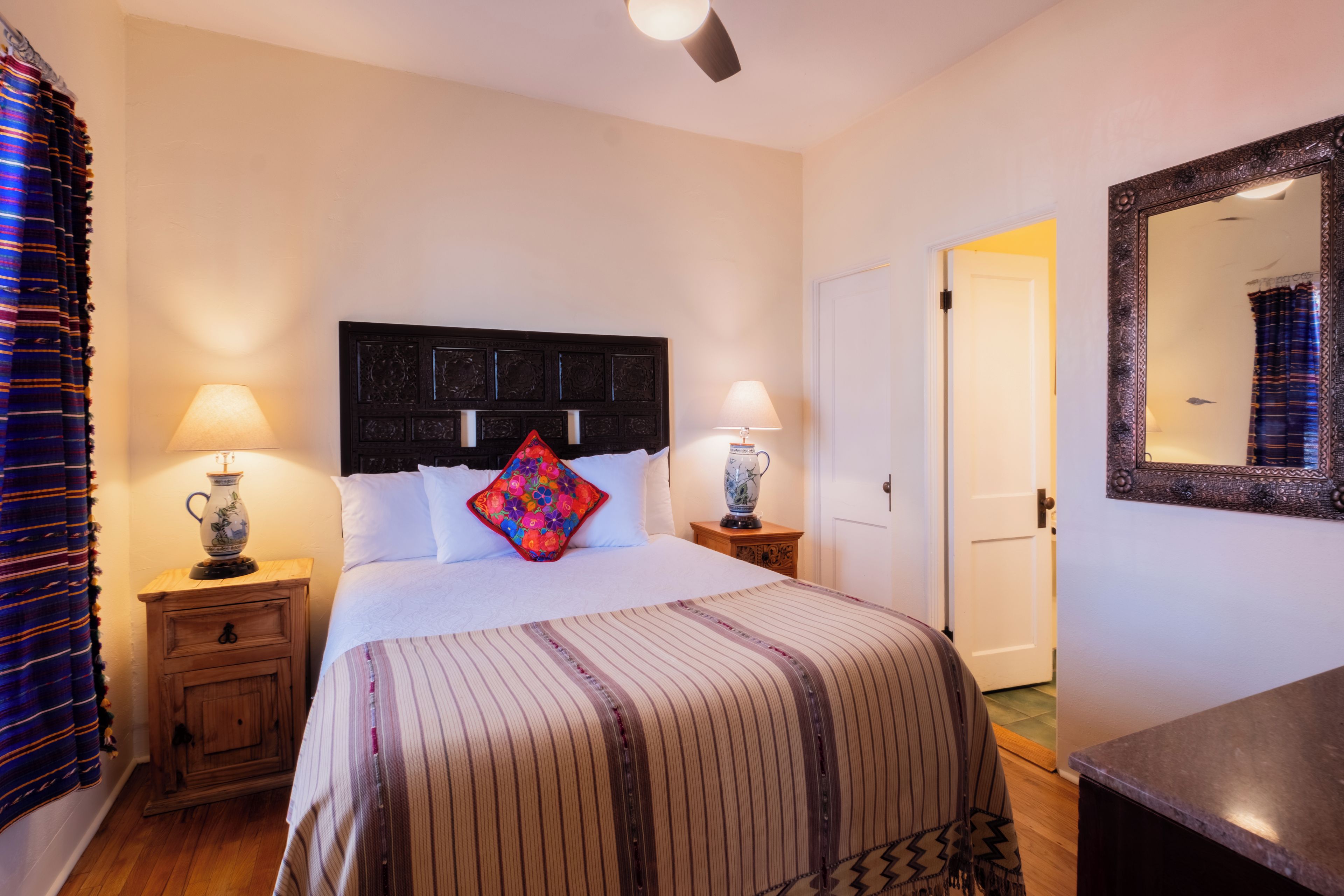 A hotel room with a bed, two bedside lamps, a nightstand, a wooden cabinet, a mirror, and a door.