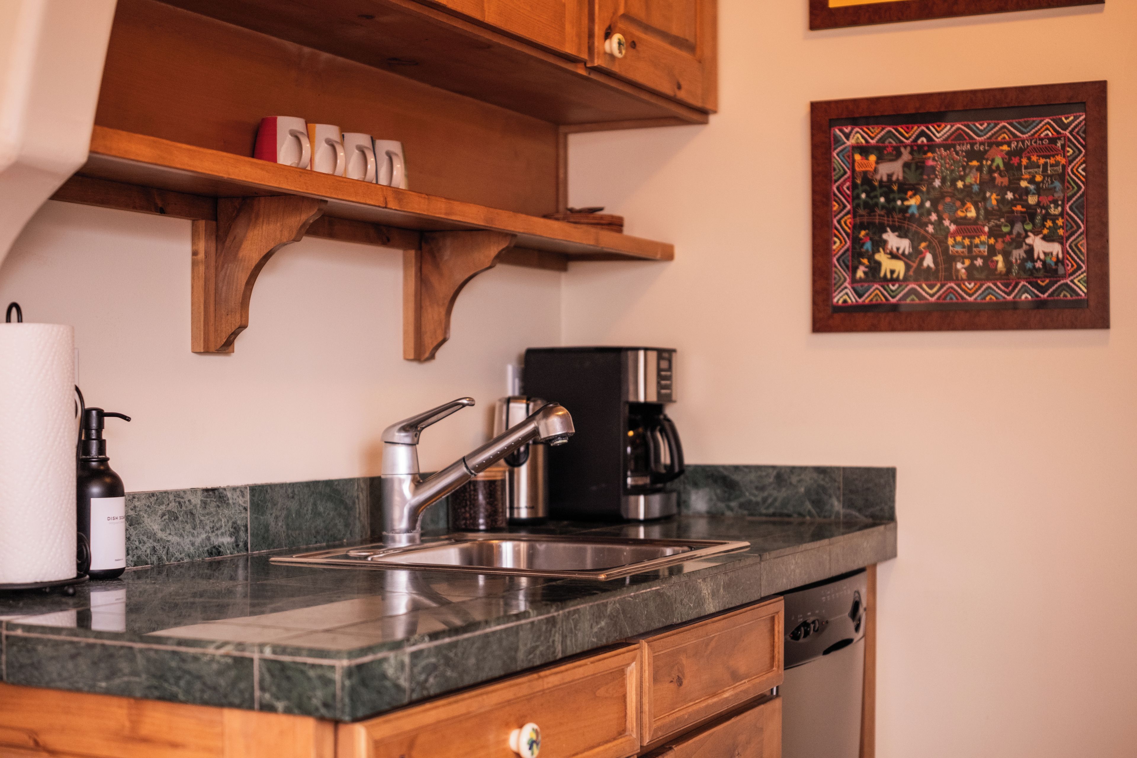 A kitchen with a stainless steel sink, a coffee maker, and wooden cabinets.