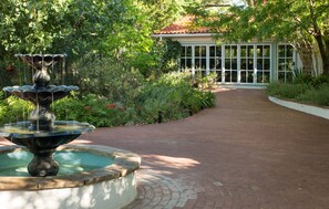 A garden with a fountain, a brick pathway, and a building with large windows. - Casa Blanca Inn (Farmington)