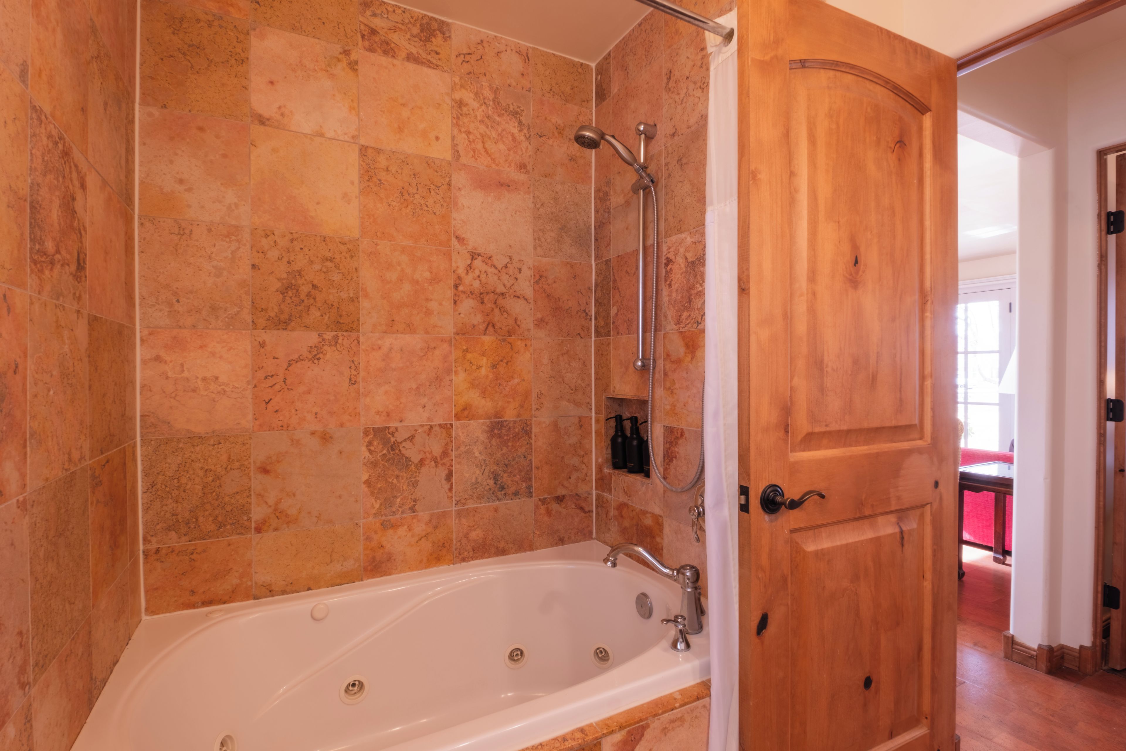 A bathroom with a bathtub, shower, and wooden door.