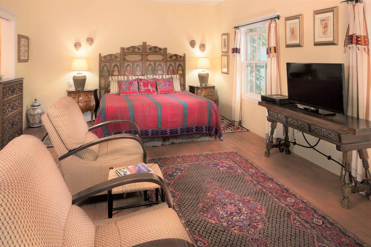 A traditional bedroom with a bed, two chairs, a television, and a decorative rug.
