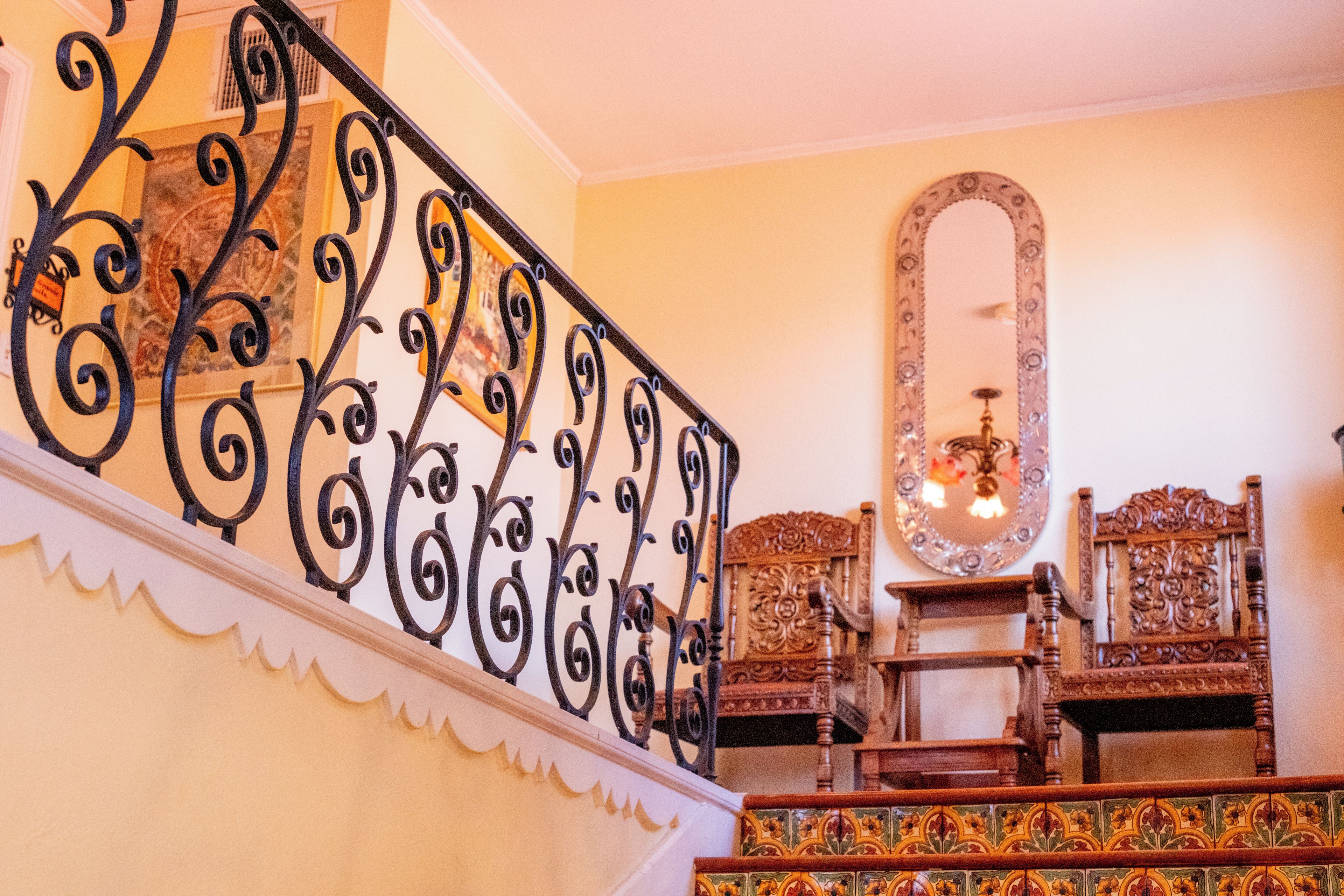 A staircase with ornate black metal railings, a wooden chair, and a mirror on the wall.