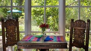 Una mesa de madera con un jarrón de flores rojas, dos sillas y manteles coloridos.