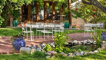 An outdoor seating area with a brick pathway, white metal chairs, and a small water feature with rocks.