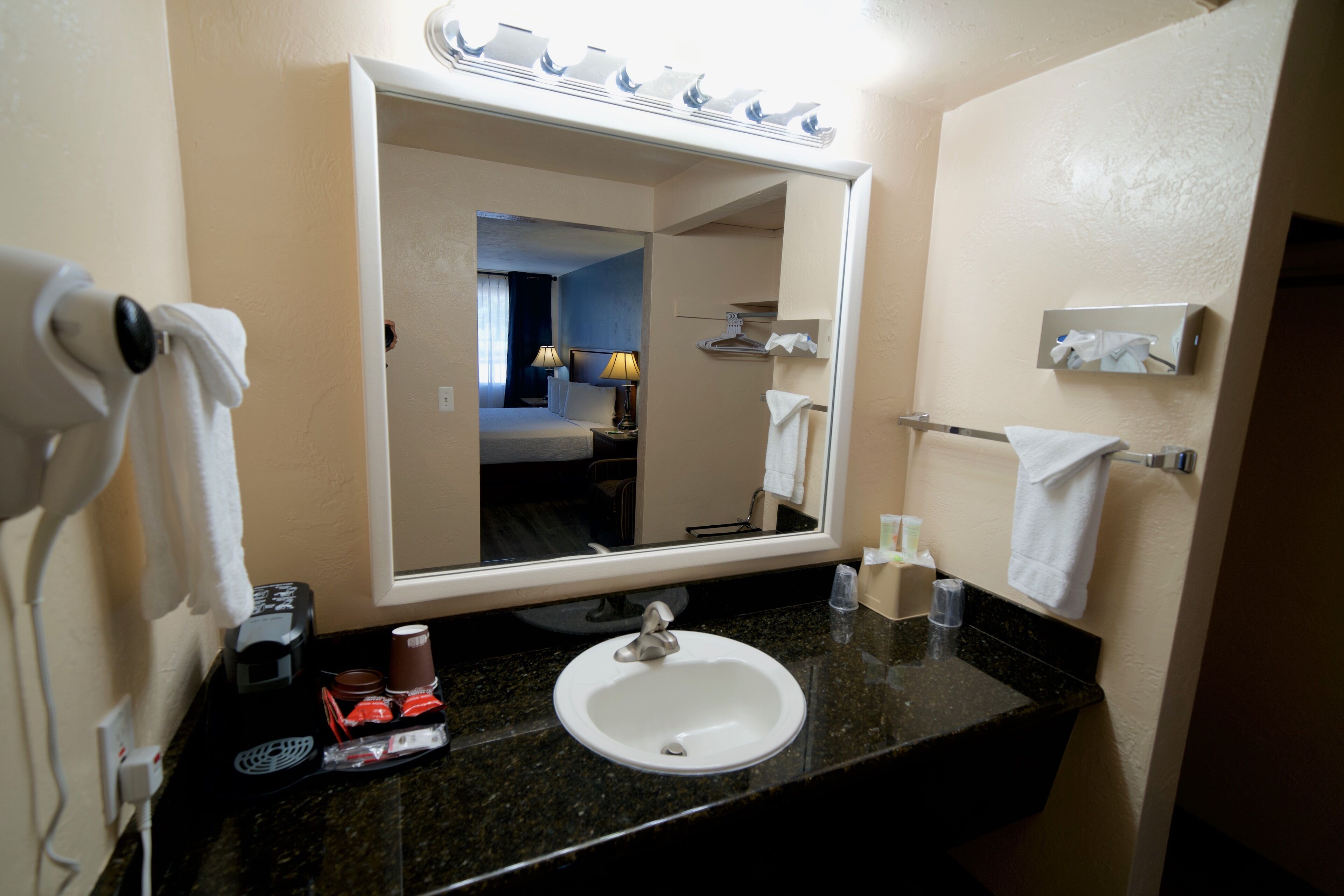 A hotel bathroom with a sink, mirror, towel rack, and a hairdryer.