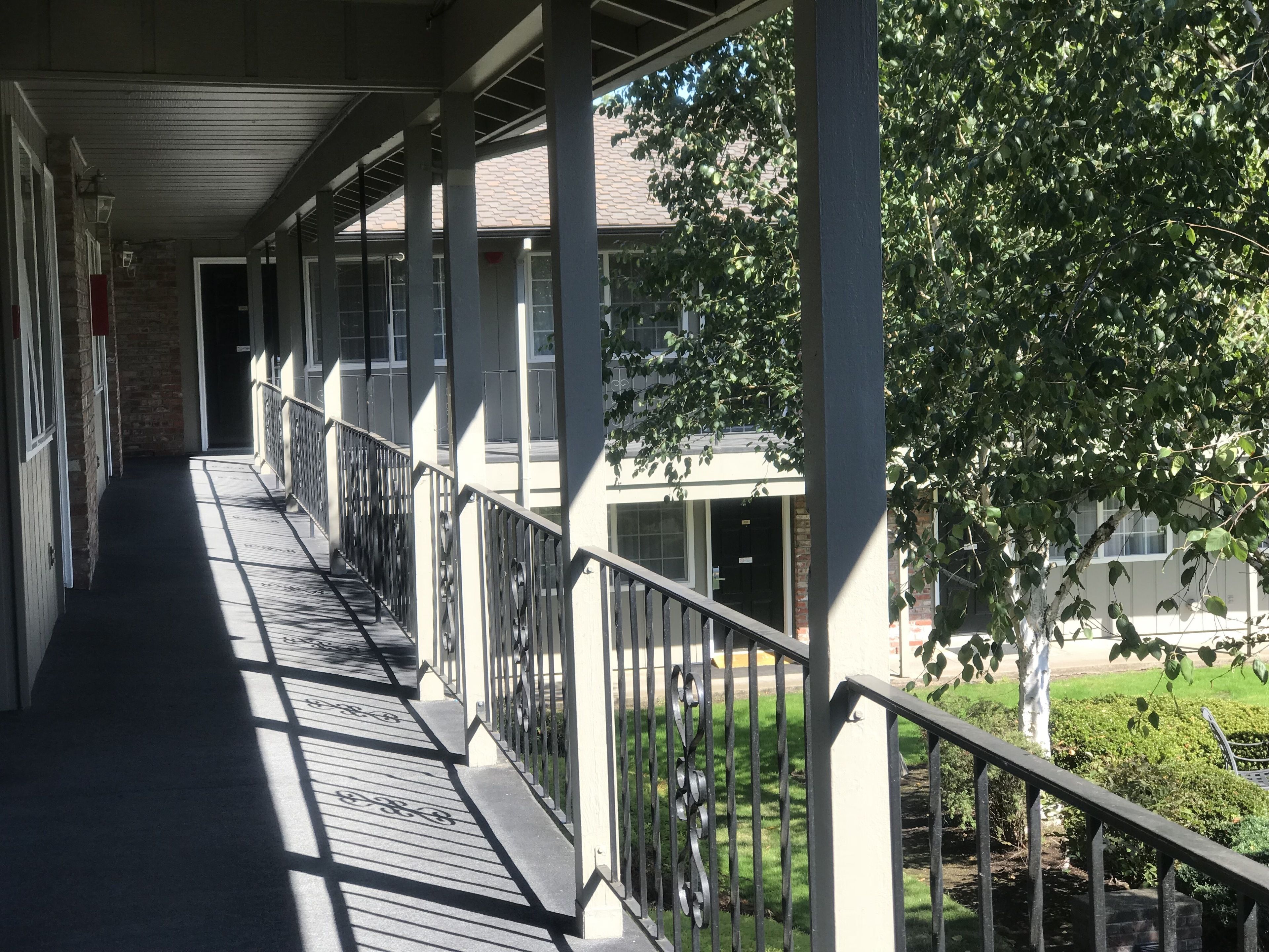 A covered outdoor corridor with a metal railing, leading to a building entrance.