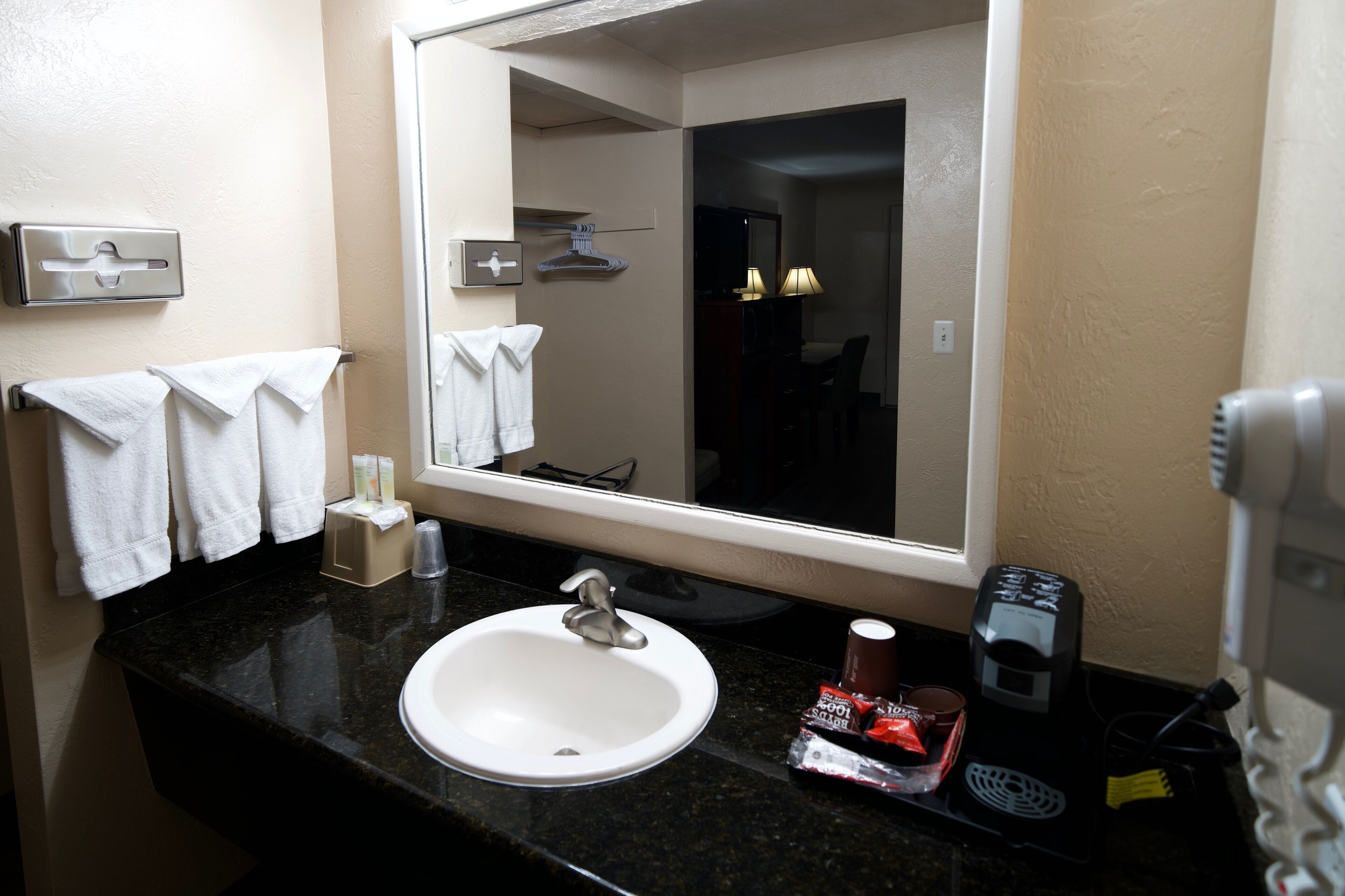 Un bagno d'albergo con lavandino, specchio, portasciugamani e articoli da toilette.