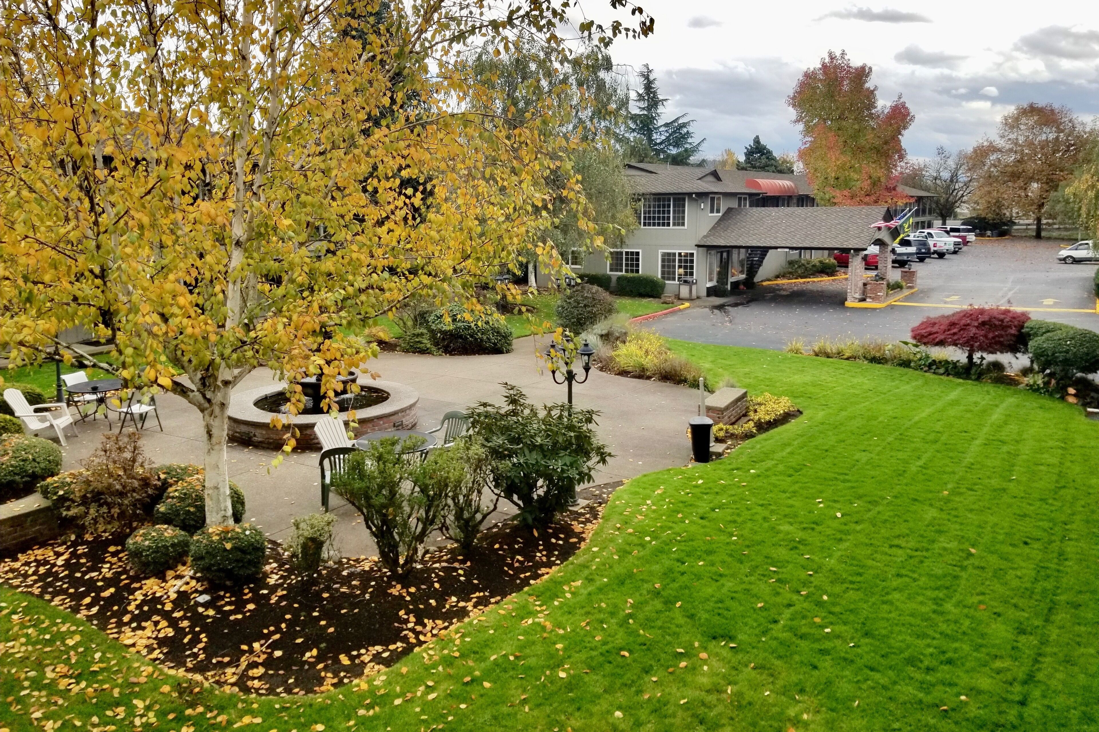 A hotel with a parking lot, a covered outdoor seating area, and a well-maintained lawn.