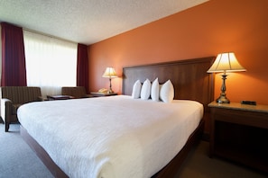 A hotel room with a large bed, two bedside tables, a chair, and a lamp.