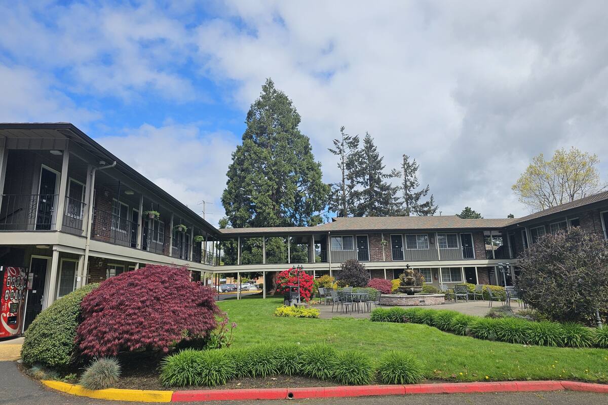 A building with a covered outdoor area, a lawn, and a large tree.