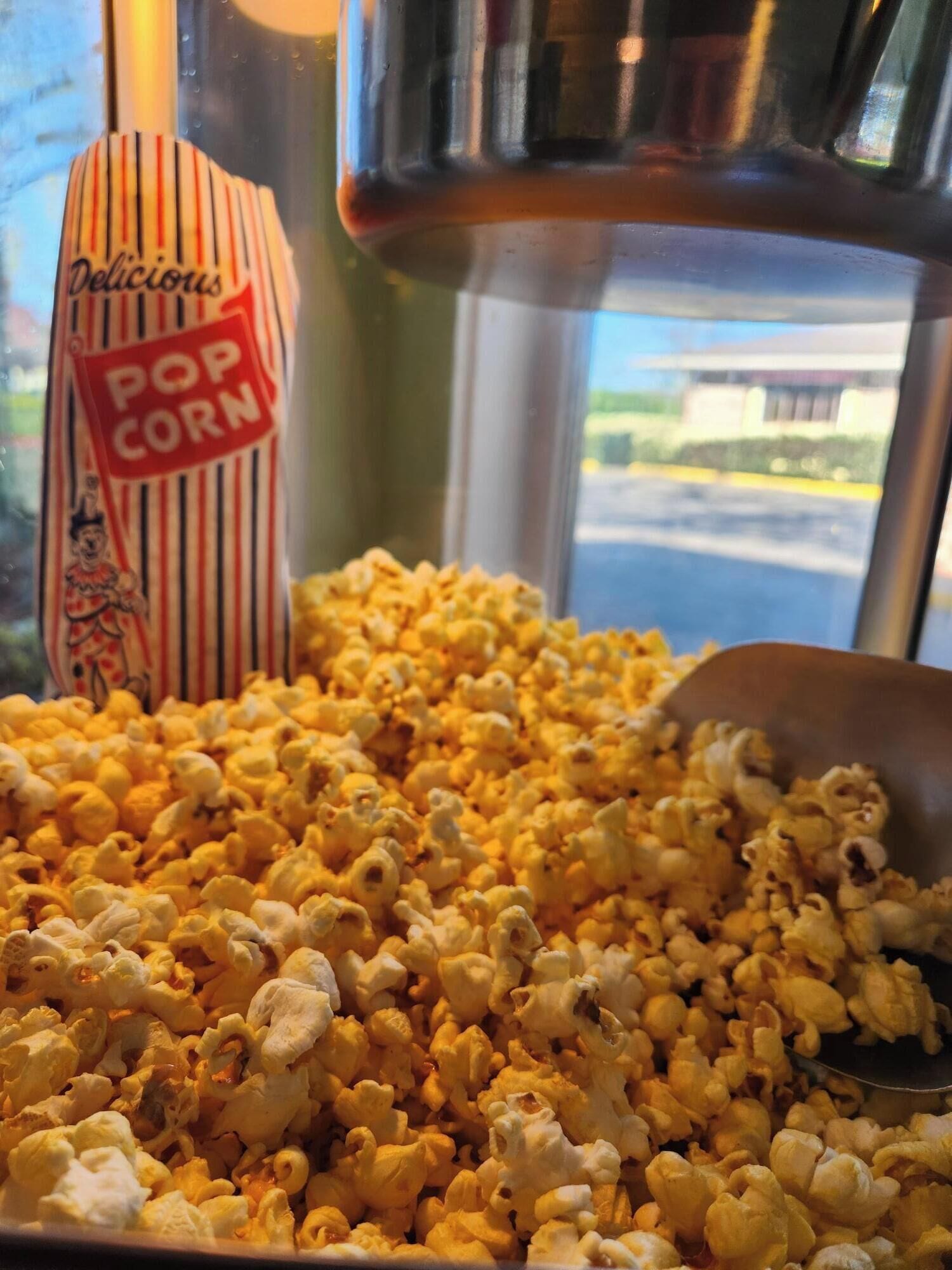 Un grand récipient rempli de pop-corn, un sac à rayures portant l’inscription « Pop-corn délicieux », et une cuillère.