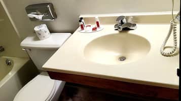 A bathroom with a toilet, sink, and bathtub. There is a towel dispenser, a soap dispenser, and a hand dryer.