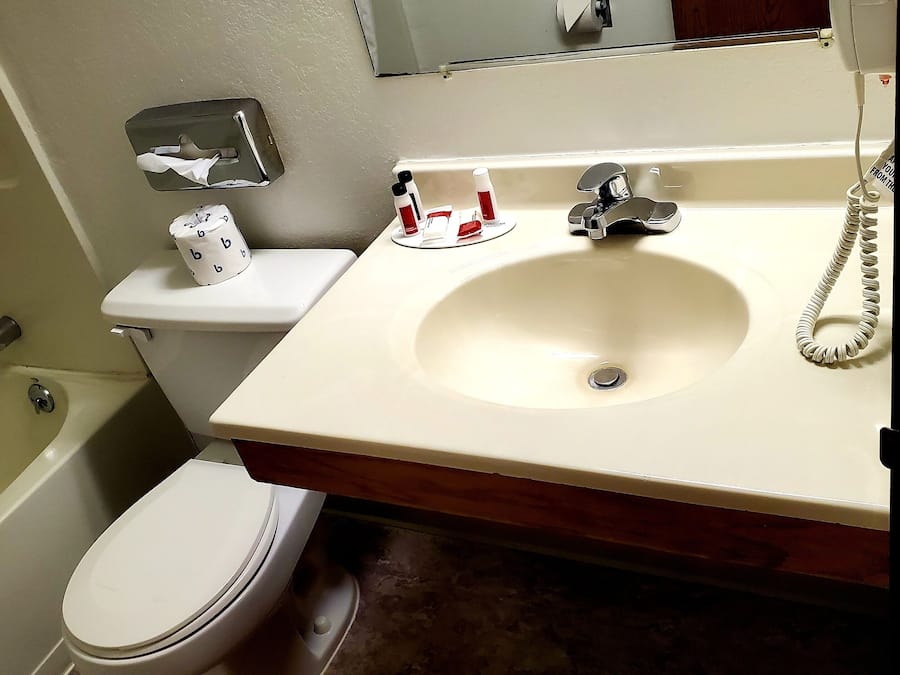 A bathroom with a toilet, sink, and bathtub. There is a towel dispenser, a soap dispenser, and a hand dryer.