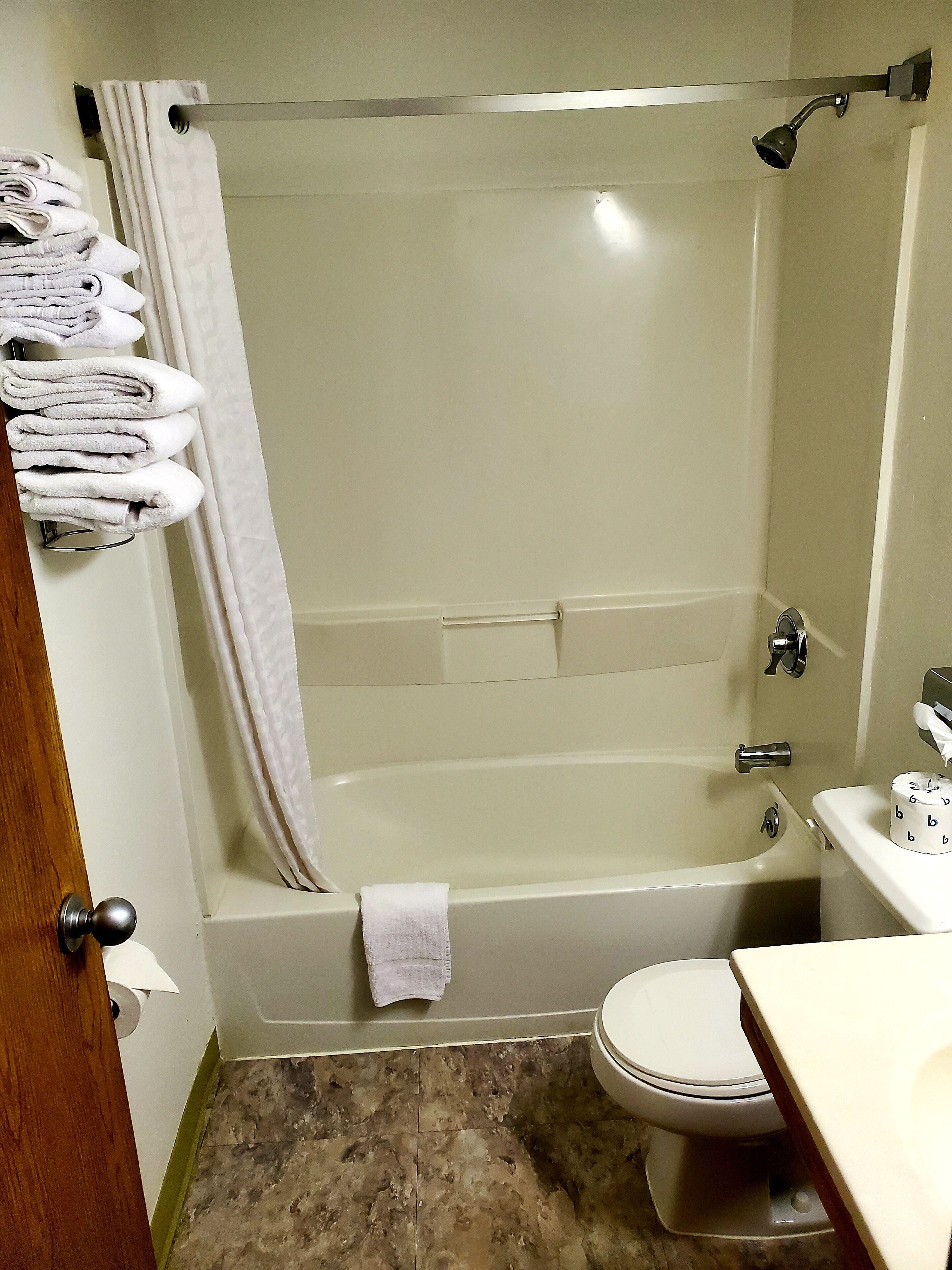 A bathroom with a bathtub, toilet, and a towel rack with folded towels.