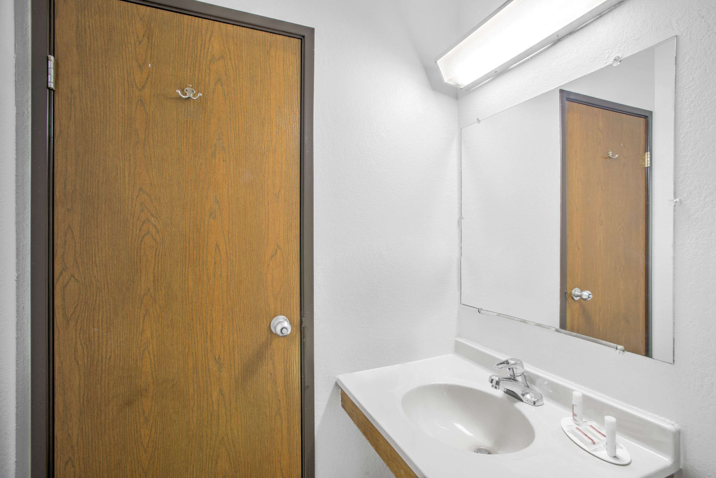 A bathroom with a wooden door, a white sink, and a mirror above it.