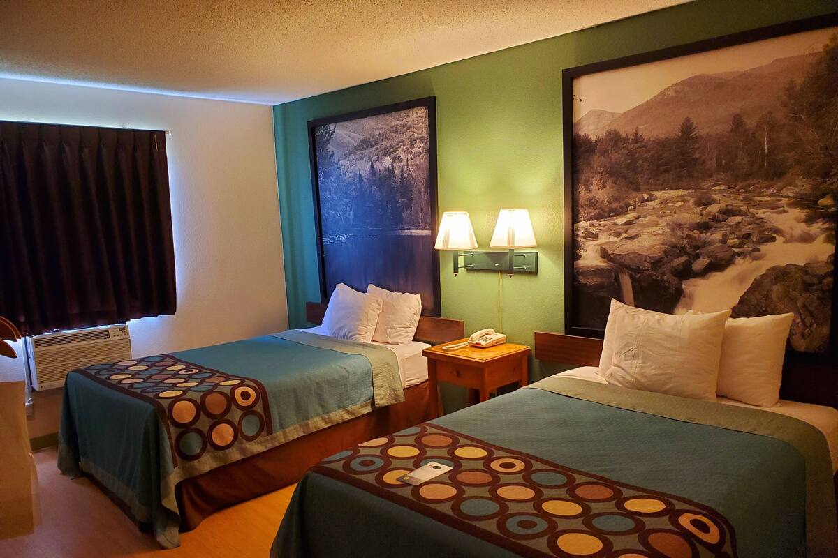 A hotel room with two beds, a nightstand with a lamp, a telephone, and a large framed picture on the wall.