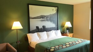 A hotel room with a bed, two lamps, a chair, and a large framed picture of a lake.