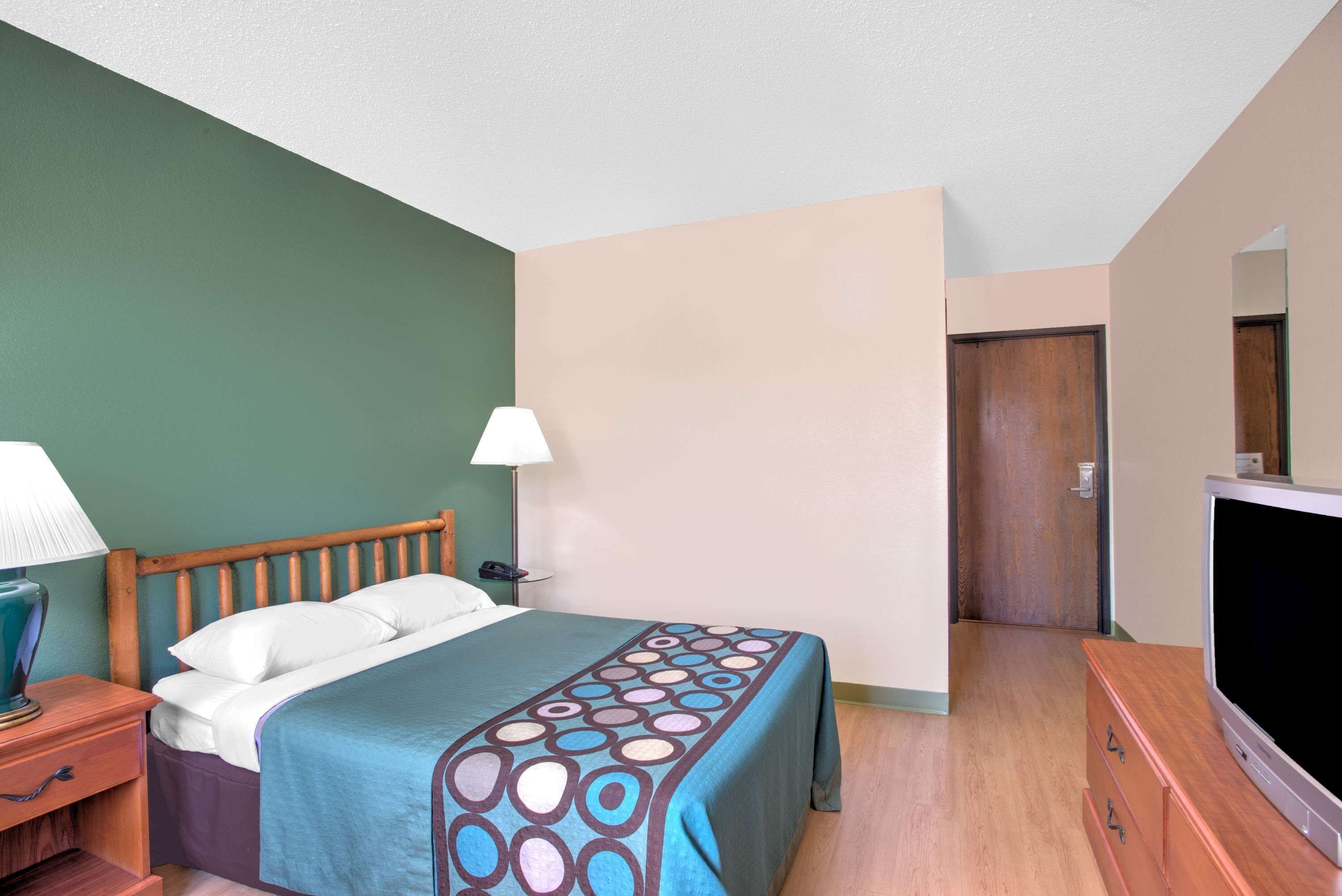 Une chambre d’hôtel comprenant un lit, une table de chevet, une lampe, une télévision et une porte donnant sur une autre pièce.