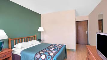 A hotel room with a bed, bedside table, lamp, TV, and a door leading to another room.