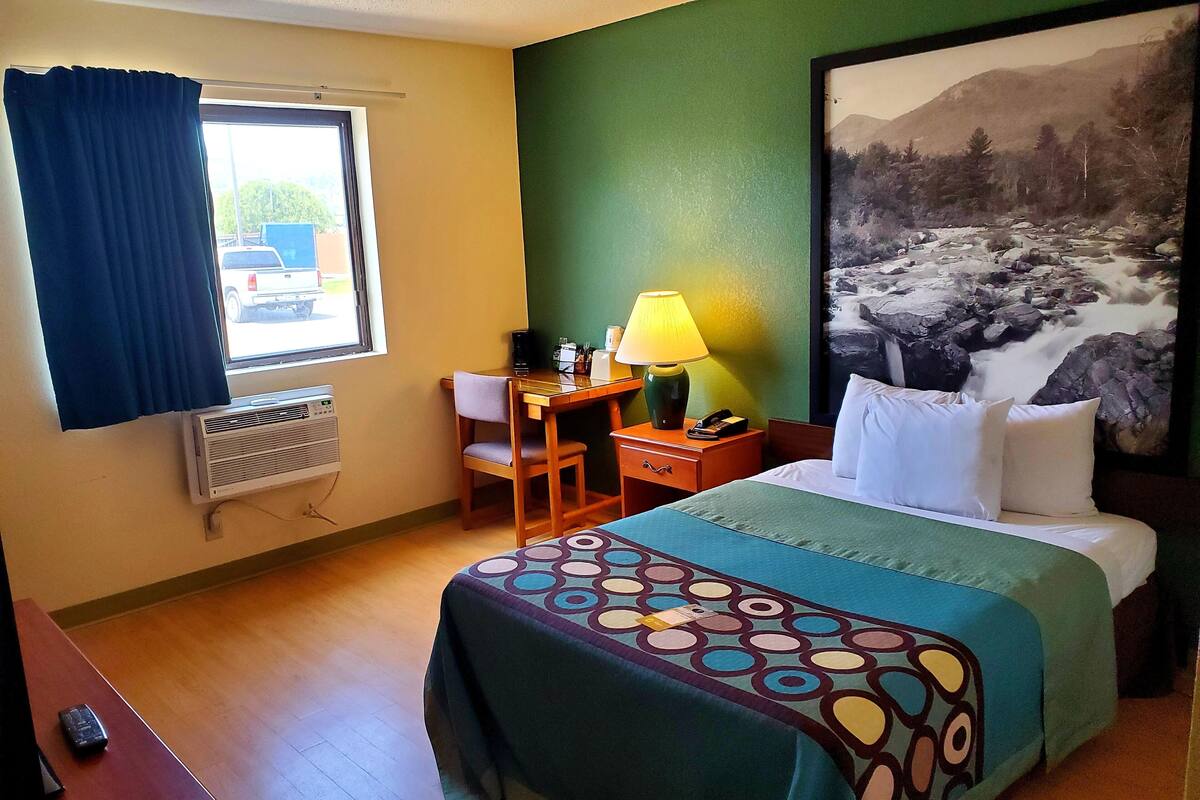 A hotel room with a bed, a desk, a chair, a lamp, and a large painting on the wall.