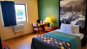Habitación de hotel con cama, escritorio, silla, lámpara y un cuadro grande en la pared.