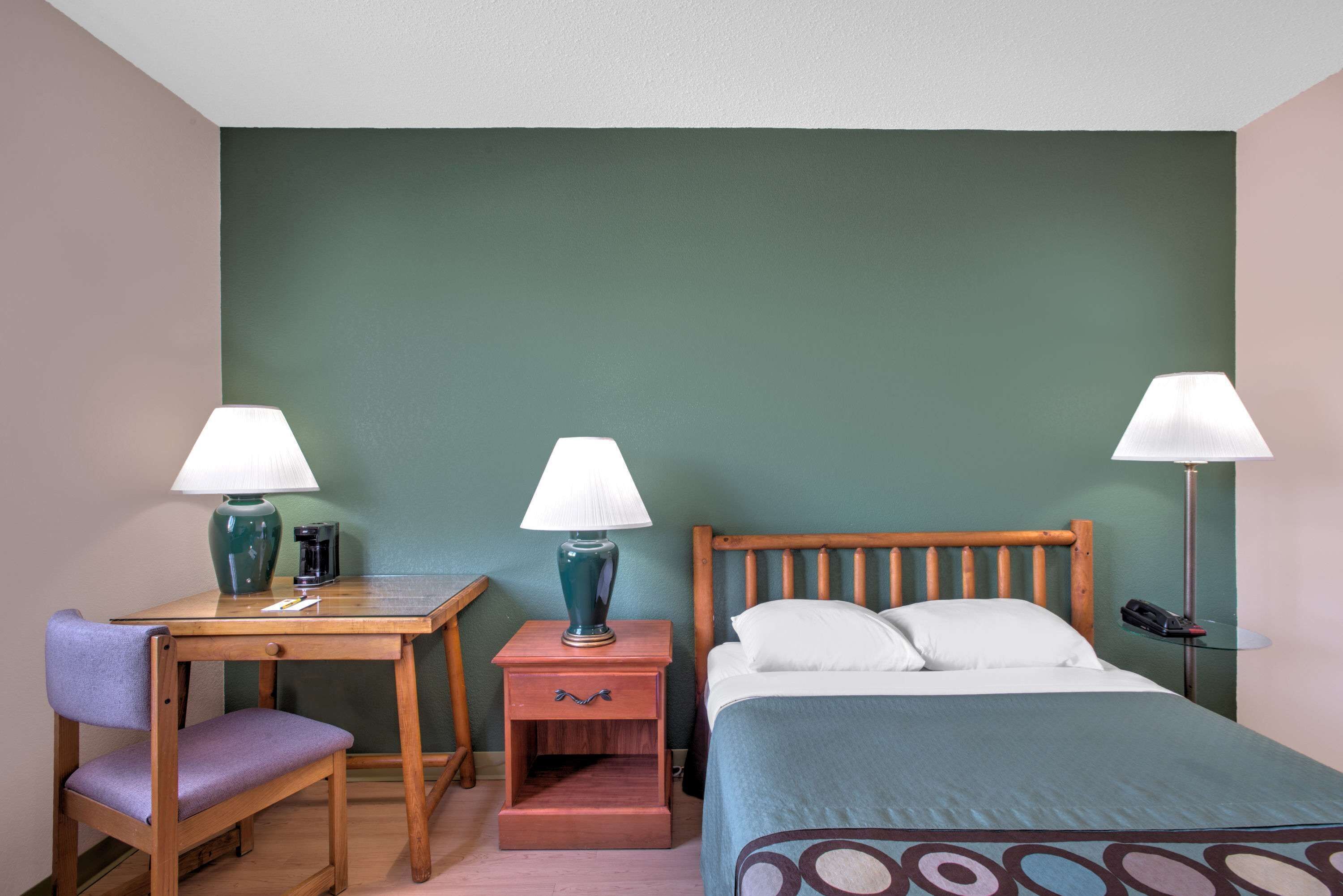 Una habitación de hotel con cama, escritorio, silla, mesita de noche y dos lámparas.