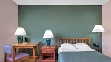 Una habitación de hotel con cama, escritorio, silla, mesita de noche y dos lámparas.