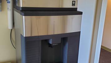 Dispensador de agua de acero inoxidable con tapa negra y un botón para dispensar agua.