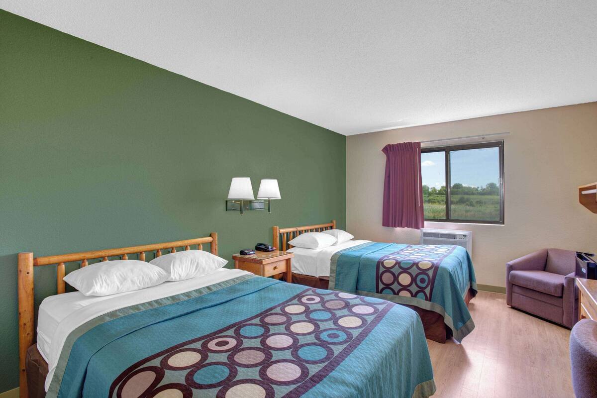 A hotel room with two beds, a window with a view, a chair, and a nightstand with a lamp.