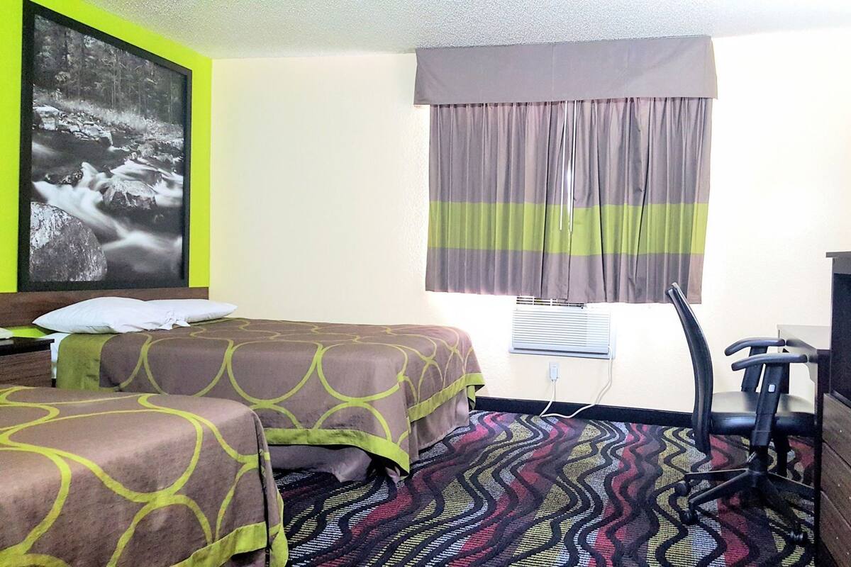 Ein Hotelzimmer mit zwei Betten, einem Fernseher, einem Schreibtisch und einem Fenster mit Vorhängen.