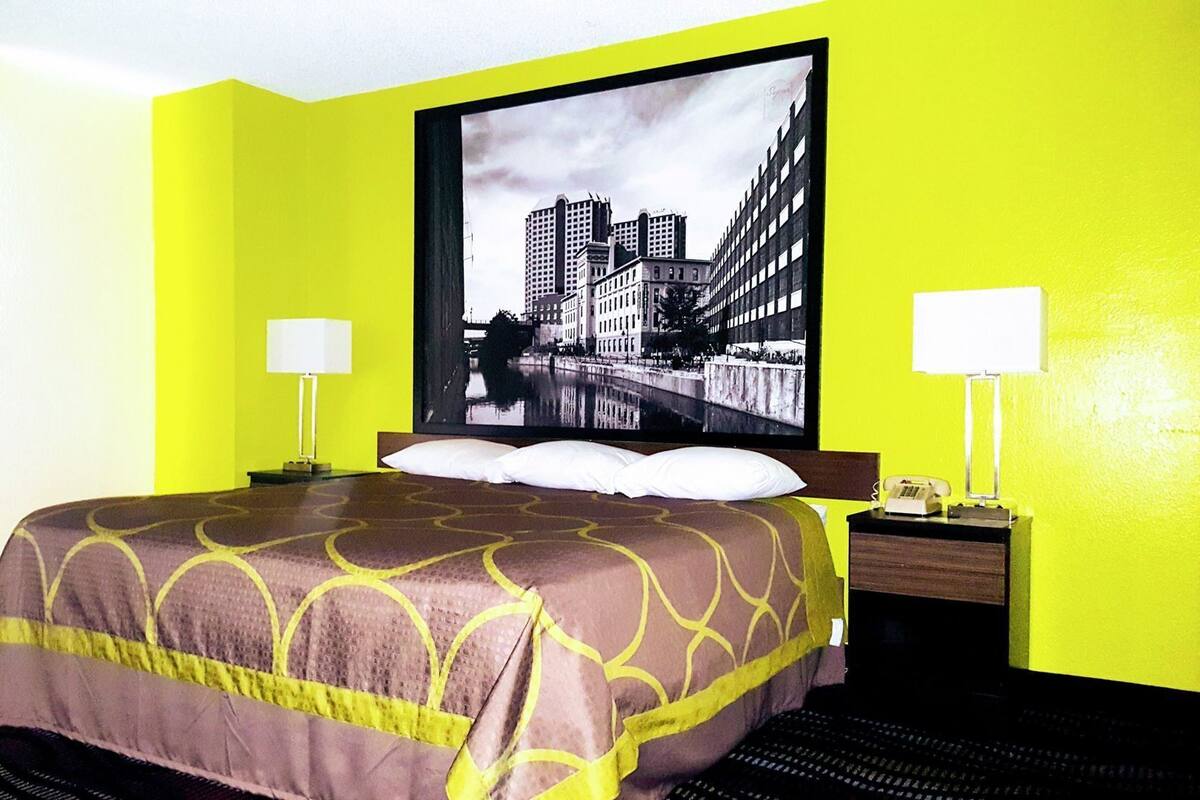 Ein Hotelzimmer mit einem Bett, zwei Nachttischlampen, einem Nachttisch und einem großen Stadtbild an der Wand.