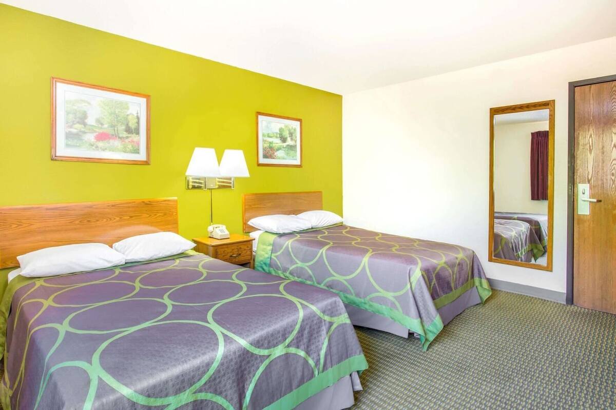 Ein Hotelzimmer mit zwei Betten, einem Nachttisch mit Lampe und einem Spiegel.
