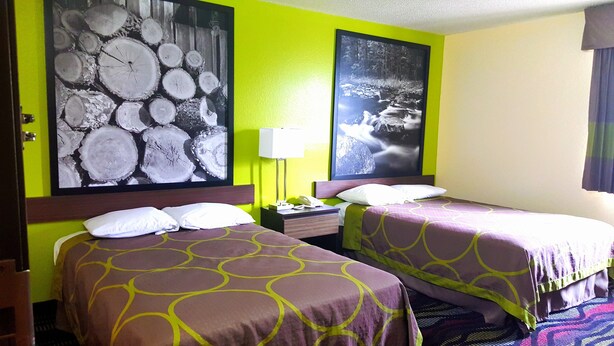 Une chambre d’hôtel avec deux lits, une table de chevet, une lampe et deux grandes œuvres d’art murales.