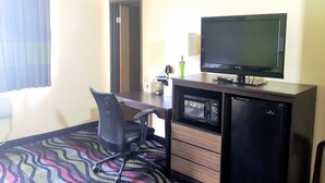 Une chambre d’hôtel équipée d’un bureau, d’une chaise, d’une télévision, d’un four à micro-ondes et d’un réfrigérateur.