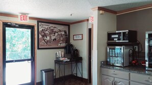 Une pièce avec un panneau indiquant la sortie, une affiche de bienvenue encadrée, une kitchenette équipée d’un four à micro-ondes et une poubelle.