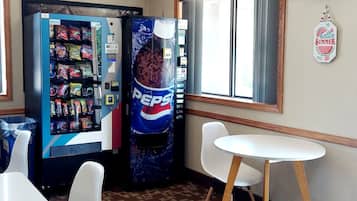 A room with two vending machines, one with snacks and one with beverages, a white table, and two white chairs.