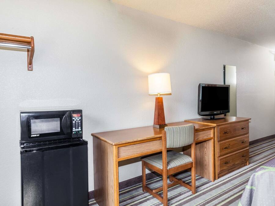 Ett hotellrum med ett skrivbord i trä, en tv, en mikrovågsugn, en stol och en lampa.