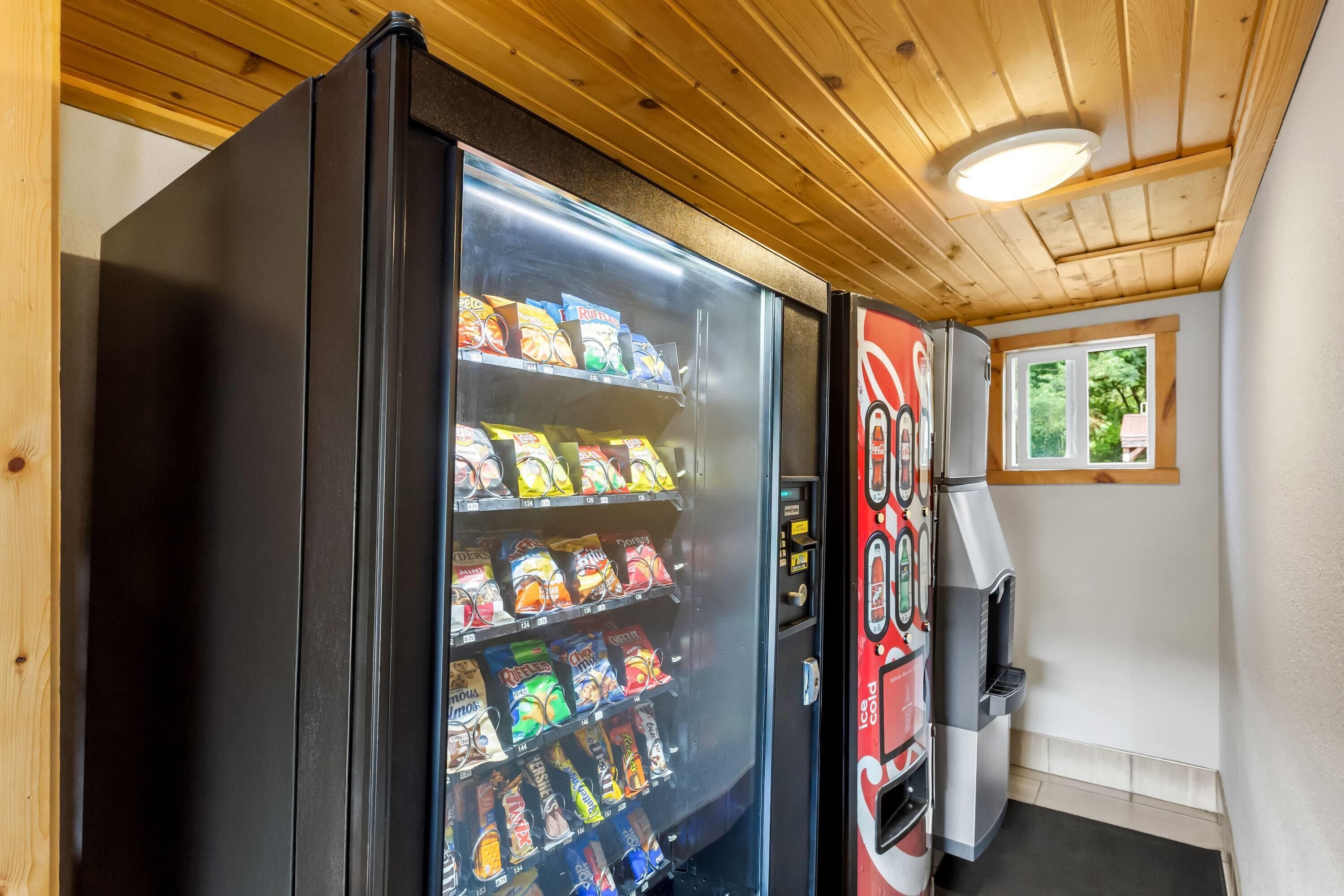 Máquina automática de snacks e dispensador de Coca-Cola em um quarto com teto de madeira e janela.