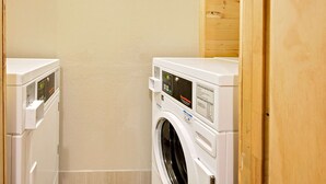 A laundry room with two stacked washers and dryers, wooden walls, and a tiled floor. - Super 8 by Wyndham Elkins (Elkins)