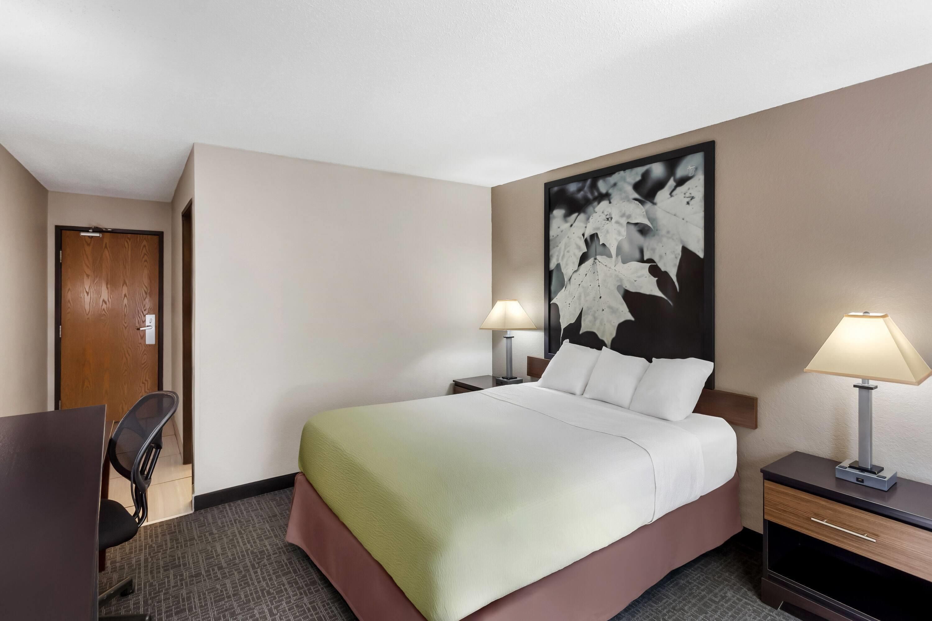 A hotel room with a bed, two bedside lamps, a desk, and a chair.