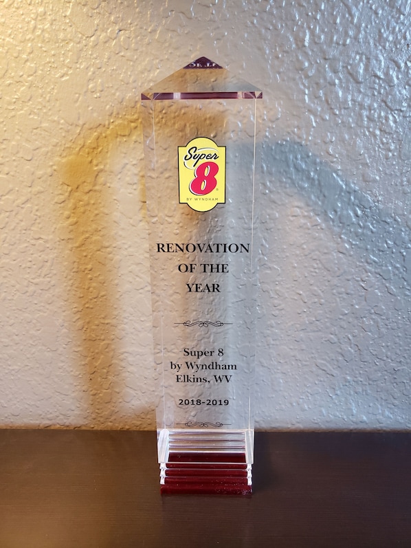 Una placa conmemorativa de acrílico transparente con el texto "Super 8 by Wyndham Elkins, WV 2018-2019" sobre un fondo de pared texturizada.