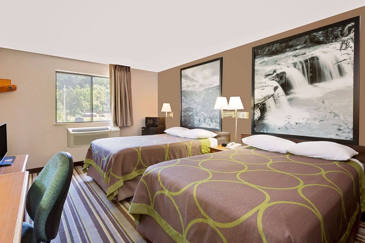 A hotel room with two beds, a desk, a chair, a large window, and a waterfall painting.