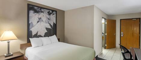 Una habitación de hotel con cama, mesita de noche, lámpara y un cuadro abstracto grande en la pared.