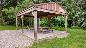 Un belvédère en bois, doté d’un banc et d’une table de pique-nique, entouré de gravier et d’herbe, situé dans un espace boisé.